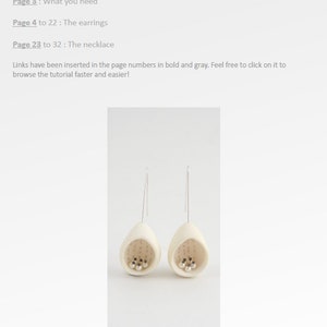 May include: A pair of white ceramic earrings shaped like eggs with small silver beads inside. The earrings are hanging from silver hooks.