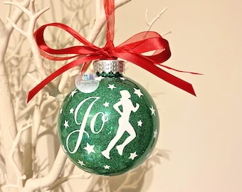 Puede incluir: Adorno navideño de purpurina verde con una silueta de corredor blanca y la palabra "Jo" en cursiva. El adorno está decorado con estrellas blancas y tiene una cinta roja.