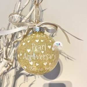 May include: Gold glitter Christmas ornament with white hearts and the text "Mum and Dad Pearl Anniversary 20.10.90".