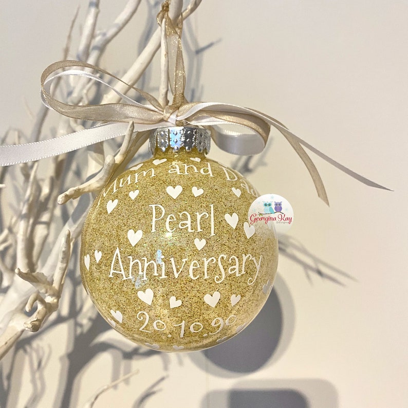 May include: Gold glitter Christmas ornament with white hearts and the text "Mum and Dad Pearl Anniversary 20.10.90".