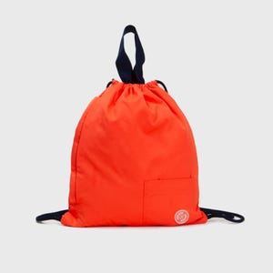 Könnte beinhalten: Eine leuchtend orangefarbene Kordeltasche mit einem dunkelblauen Kordelzug und einer kleinen Tasche auf der Vorderseite. Die Tasche hat ein weißes Logo mit dem Text "The Original" und einem Kreis.