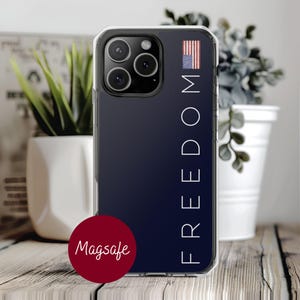 May include: Clear phone case with a navy blue background. The word "FREEDOM" is printed vertically in white, with an American flag graphic. A red circle with the word "Magsafe" is at the bottom.
