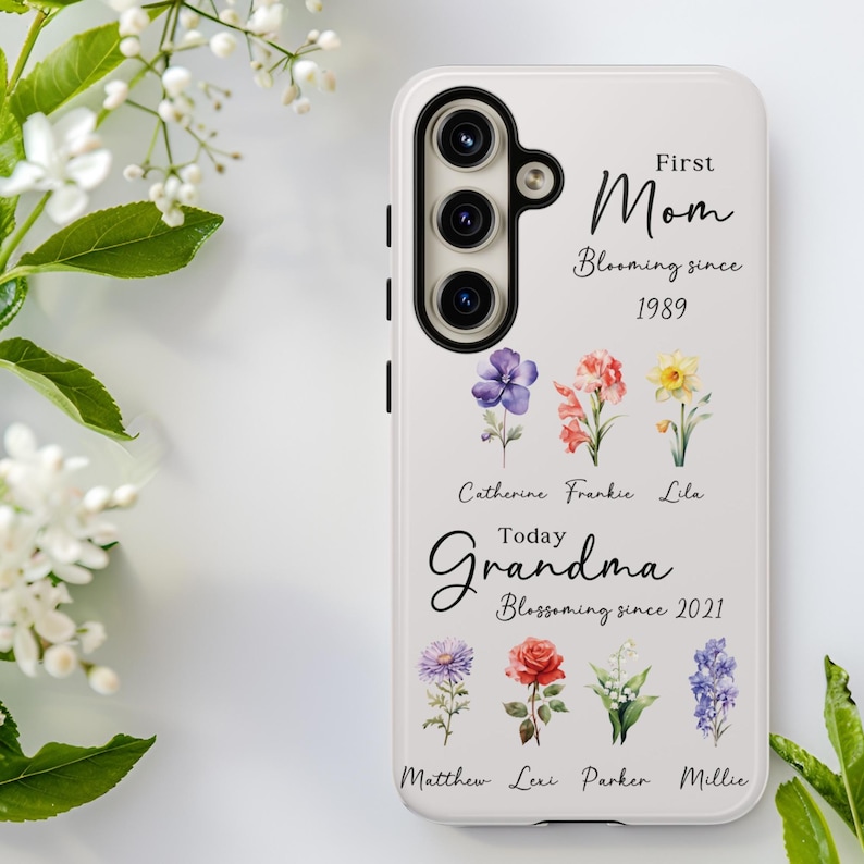 May include: White phone case with a floral design and the words "First Mom Blooming since 1989" and "Today Grandma Blossoming since 2021". The case features a camera and several colorful flower illustrations.