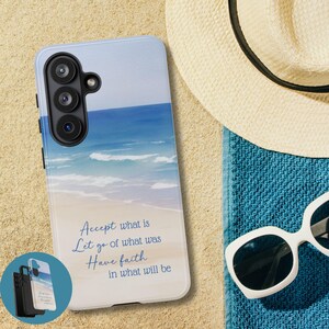 May include: A smartphone case featuring a beach scene with blue ocean waves, a sandy shore, and a light blue sky. The case has the text "Accept what is, Let go of what was, Have faith in what will be." A straw hat, sunglasses, and a blue towel are also visible.
