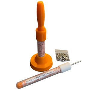 May include: Orange paper bead crafting tools, including a handle, a tube with text, and a bag of metal rings. The tube is labeled "#2 3/32" - 2.38mm - Paper Bead Crafts". The handle has a round base.