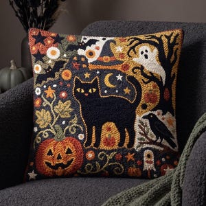 Può includere: Un cuscino quadrato con un dettagliato design a punch needle che raffigura un gatto nero centrale, una grande zucca arancione, un fantasma bianco, un corvo nero, un cappello da strega, stelle e una mezzaluna su sfondo scuro.