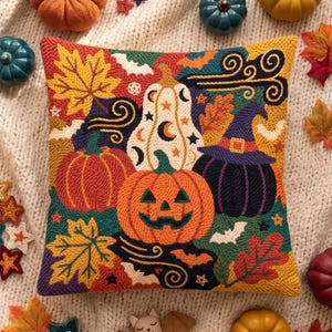 May include: A square throw pillow featuring a punch needle design of a jack-o'-lantern, a witch-hat-wearing pumpkin, and a patterned gourd surrounded by autumn leaves, bats, and stars, set against a cream-colored knitted background.
