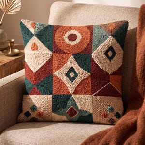 Op de afbeelding: Een vierkant sierkussen met een getextureerd punch needle ontwerp met een geometrisch patroon in roestoranje, crème en donkerblauwgroen. Het oppervlak toont diverse vormen, waaronder cirkels, ruiten en driehoeken in een raster.