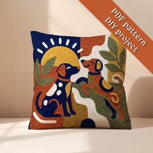 May include: A square punch needle cushion cover featuring a colorful graphic design of two dogs, a yellow sun, and green foliage. The text PDF pattern - DIY project is printed in the upper right corner. The design uses navy, orange, and white.
