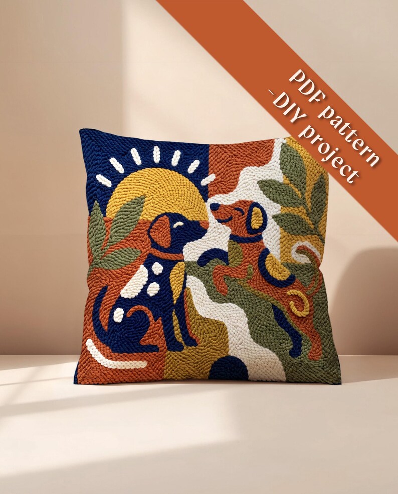May include: A square punch needle cushion cover featuring a colorful graphic design of two dogs, a yellow sun, and green foliage. The text PDF pattern - DIY project is printed in the upper right corner. The design uses navy, orange, and white.