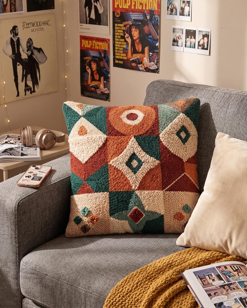 May include: A square throw cushion featuring a textured punch needle design with a geometric pattern. The surface displays a mix of cream, burnt orange, and deep teal yarn in various shapes including diamonds, circles, and triangles.