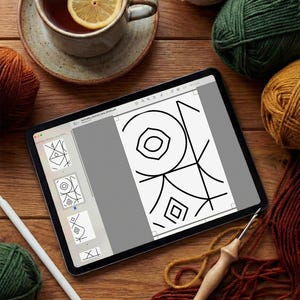 May include: A tablet displaying a digital geometric pattern design, surrounded by several balls of yarn in shades of beige, green, orange, and brown, a wooden crochet hook, a white stylus, and a ceramic mug containing tea with a lemon slice.