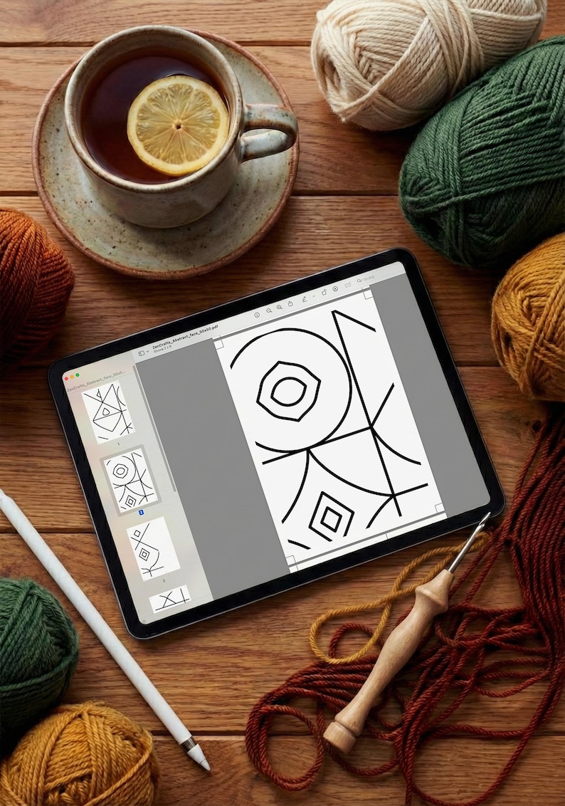 May include: A tablet displaying a digital geometric pattern design, surrounded by several balls of yarn in shades of beige, green, orange, and brown, a wooden crochet hook, a white stylus, and a ceramic mug containing tea with a lemon slice.