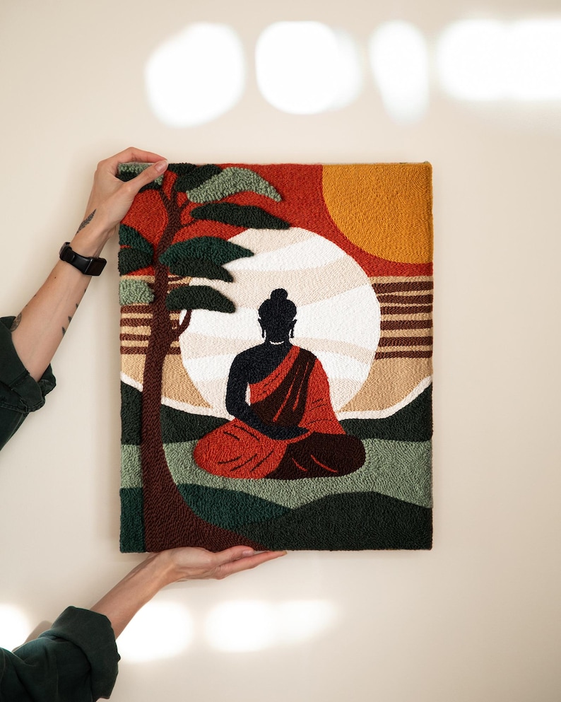 May include: A colorful needlepoint wall hanging featuring a silhouette of Buddha meditating under a large sun with a palm tree in the background.