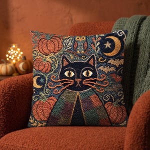 May include: A square throw pillow featuring a punch needle design of a black cat with yellow eyes and orange whiskers. The background includes orange pumpkins, a small owl, a crescent moon with a star, and bats against a dark blue backdrop.