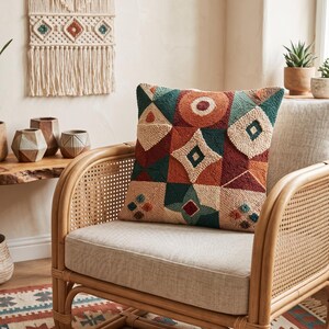 May include: A square throw cushion featuring a textured punch needle design with a geometric pattern in shades of terracotta, dark teal, and cream. The cushion displays various shapes including circles, diamonds, and triangles across its surface.