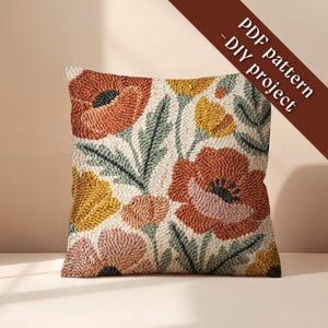 Op de afbeelding: Vierkant decoratief kussen met een bloemenontwerp met oranje, gele en roze bloemen met groene bladeren op een witte achtergrond. Het kussen heeft een getextureerde uitstraling. Tekst op de afbeelding luidt "PDF pattern - DIY project."