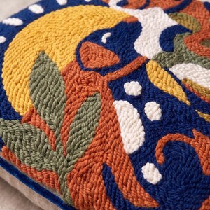 May include: A square throw pillow featuring a textured punch needle design with a vibrant pattern of abstract shapes in shades of deep blue, mustard yellow, terracotta orange, sage green, and white, finished with a dark blue velvet piping edge.
