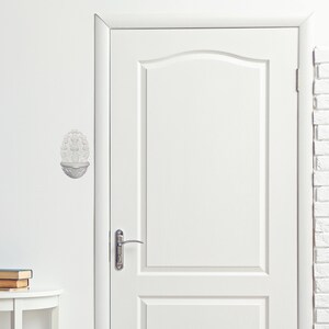 May include: A white wall-mounted decorative sculpture featuring a floral design. The sculpture is mounted on a white wall next to a white door. The door has a silver handle and a simple design.