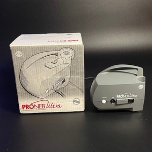 May include: A gray PARI PRONEB Ultra compressor nebulizer system with a white filter and a black on/off switch. The box for the nebulizer is also shown in the image. The box is white with red text and a picture of the nebulizer.