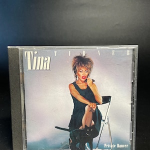 May include: A compact disc case with a photo of Tina Turner on the front. She is wearing a black dress and sitting on a chair with a black cat. The text "Tina Turner" and "Private Dancer" are printed on the case.