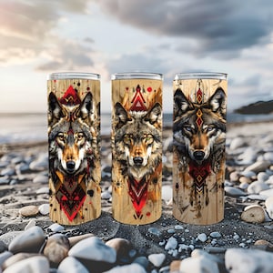 May include: Three stainless steel tumblers with a wood grain finish and a wolf design. Each tumbler features a different geometric pattern and a wolf with a different color scheme. The tumblers are on a bed of small rocks.
