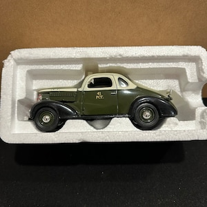 Puede incluir: Un coche de modelo en una vitrina. El coche es de color verde oscuro con techo crema y guardabarros negros. El texto "41 PCT." está impreso en el lateral. El coche está en un inserto de espuma blanca.