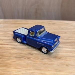 Puede incluir: Un pequeño modelo de fundición a presión de una camioneta azul clásica. El camión de juguete presenta un interior detallado, detalles cromados y una caja blanca. El modelo es de estilo vintage.