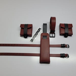 May include: A set of burgundy leather accessories, including a belt, pouches, and straps. The pouches and belt feature black accents. The set includes a holster and is designed for a costume or cosplay. The text "OFFICERSPROPS" is visible.