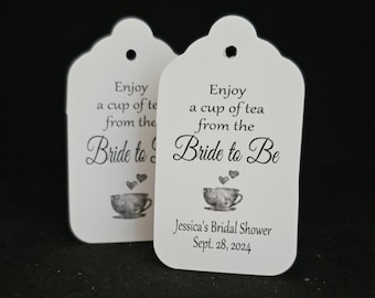 May include: Two white favor tags with black text and a teacup graphic. The text reads "Enjoy a cup of tea from the Bride to Be". One tag includes the text "Jessica's Bridal Shower Sept. 28, 2024".