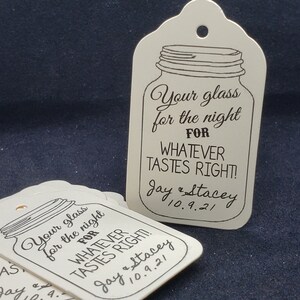May include: Two white wedding favor tags with a mason jar design. The text on the tags reads "Your glass for the night FOR WHATEVER TASTES RIGHT!" with the couple's names and wedding date below.