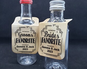 May include: Two small glass bottles with labels that say "Groom's Favorite" and "Bride's Favorite". The labels are brown with black text and include the names "Gemma & Jack" and the year "2023".