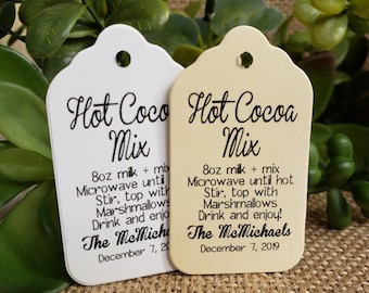 May include: Two white gift tags with black text. The tags are shaped like a teardrop with a hole at the top. The text on the tags reads "Hot Cocoa Mix" and includes instructions for making hot cocoa. The tags are dated December 7, 2019.