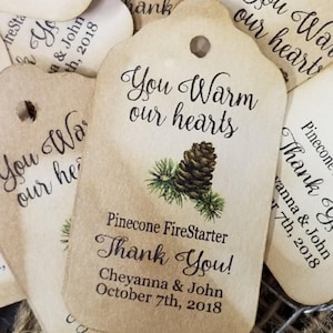 May include: Rustic brown paper gift tags with a pine cone design and the text "You Warm Our Hearts" and "Pinecone FireStarter Thank You! Cheyanna & John October 7th, 2018".