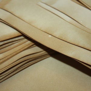 May include: A close-up of a stack of light brown paper sheets, each with a darker, aged edge. The paper has a vintage, weathered look, possibly for crafts, scrapbooking, or artistic use.