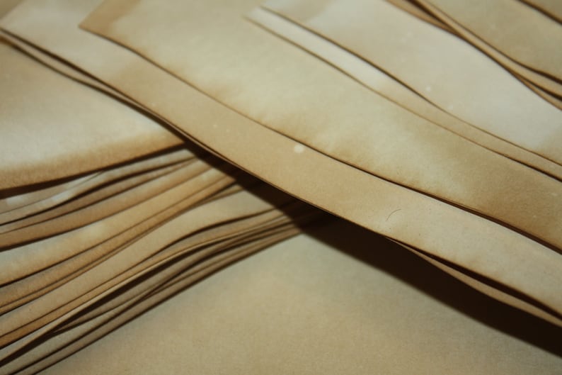 May include: A close-up of a stack of light brown paper sheets, each with a darker, aged edge. The paper has a vintage, weathered look, possibly for crafts, scrapbooking, or artistic use.