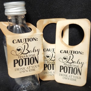 May include: Two brown paper bottle tags with a hole at the top. The tags have the text "CAUTION: Baby making POTION DRINK AT YOUR OWN RISK" printed in black.