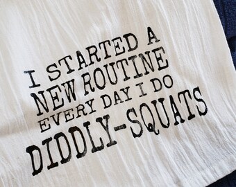 May include: White kitchen towel with black text that reads "I started a new routine every day I do diddly-squats".