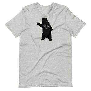 Op de afbeelding: Een grijs t-shirt met een zwart silhouet van een beer met het woord "HUG" op de borst.