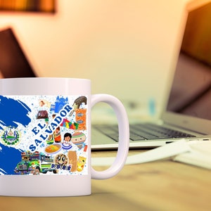 May include: White ceramic mug with a blue and white design featuring the flag of El Salvador and various cultural icons. The mug has a handle on the right side.