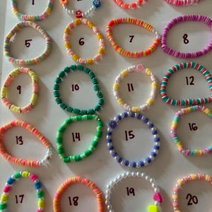 May include: A collection of twenty colorful bracelets. The bracelets feature a variety of designs, including beaded, disc-shaped, and pearl styles. Colors include pink, orange, green, yellow, and blue. Each bracelet is numbered for easy selection.