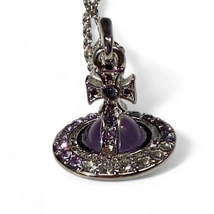 Peut inclure: Collier pendentif argenté avec un motif d'orbite violet et une croix. L'orbite est ornée de petits cristaux scintillants. La chaîne est fine. Un accessoire de mode populaire.