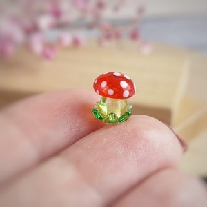 May include: A small glass mushroom figurine with a red cap with white polka dots and a green base.