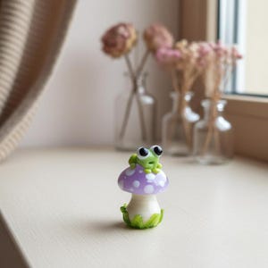 May include: A set of three ceramic mugs with a speckled, cream-colored glaze. Each mug features a different hand-painted design: a blue and green leaf, a yellow flower, and a red berry. The mugs have a simple, rounded shape.