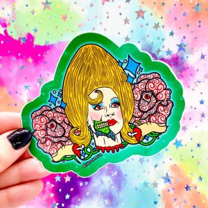 May include: A sticker featuring a cartoon illustration of a woman with a large blonde beehive hairdo. She is wearing red lipstick and has a green zombie-like creature biting her neck. The background is green with two pink roses with eyes. The sticker has the text "@pinkysdeadmium" in the bottom right corner.