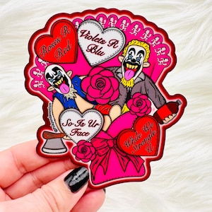 May include: A die-cut sticker with a pink and red color scheme, featuring two clown-like figures and heart-shaped text that reads "Roses R Red", "Violets R Blu", "So Is Ur Face", and "While We Strangle U". The sticker has a decorative border.