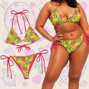 May include: A yellow and pink bikini with a graphic print of a hockey mask. The bikini top is a triangle style with adjustable straps. The bikini bottom is a cheeky style with ties on the sides.
