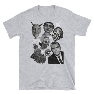 May include: A light gray t-shirt featuring a collage of black and white illustrations of various faces and figures. The graphic includes a devilish face, a ventriloquist dummy, and a man in a suit. The shirt is made of a soft material.