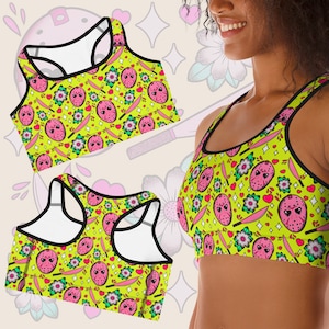 May include: A yellow sports bra with a black trim and a repeating pattern of pink and white hearts, flowers, knives, and a pink and white mask.
