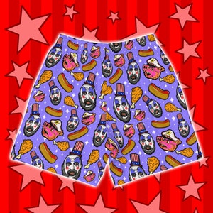 May include: Purple men's shorts with a repeating pattern of a clown wearing a red, white, and blue hat, a pig, a hot dog, and a fried chicken leg.